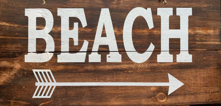 Beach sign on brown wooden background, white text met arrow - holiday vacation concept image. High quality photoの写真素材
