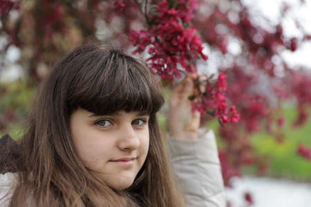 close up smiling caucasian portrait of girl, young woman outdoor, red blossom tree background in the...