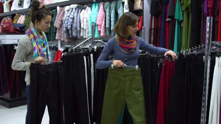 Two young beautiful girls choose clothes in a fashionable boutique. Girls carefully look at the...