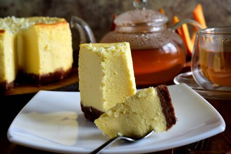 A slice of cheesecake on a white plate and a Cup of tea on a gray backgroundの写真素材