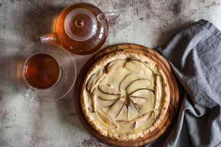 Delicious pear pie on a wooden platter, a Cup of hot tea, a teapot with tea on a gray backgroundの写真素材