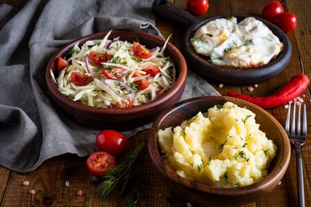 Hearty lunch: mashed potatoes in a wooden bowl, vitamin salad of vegetables in a clay plate, fried...