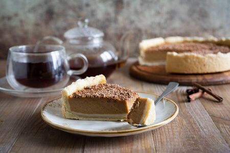 A slice of sweet pumpkin pie with cinnamon on a vintage white plate is photographed close up on a wooden tableの写真素材