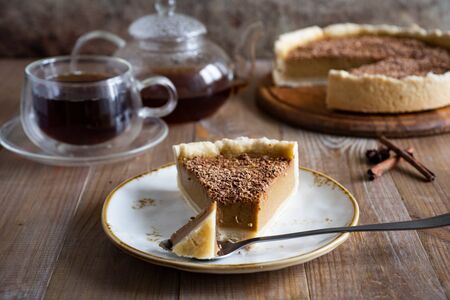 A piece of pumpkin pie on a plate, a glass Cup of tea and a pumpkin pie on a wooden platter on an old wooden tableの写真素材