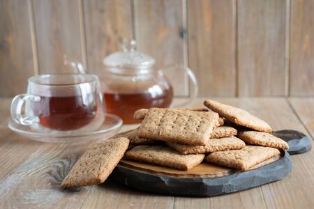 Delicious chocolate cookies in the foreground, a Cup of tea and a glass teapot with tea in the background on a wooden tableの写真素材