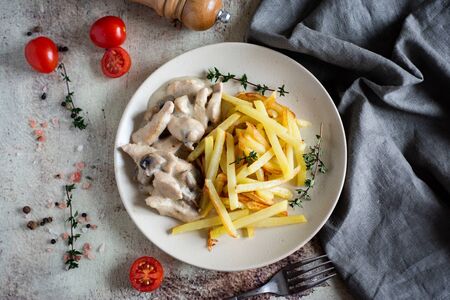 Tender chicken fricassee and French fries on a white plate on a gray background. The view from the topの写真素材