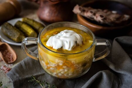 Hot soup with ribs and vegetables in a transparent plate close-up on a gray background. Pickle with sour creamの写真素材