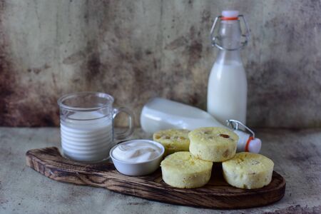 Cheesecakes with raisins on a wooden platter on a gray background. Milk bottles and a glass of milk on a grey backgroundの写真素材