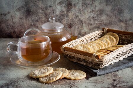 Sesame crackers in a wicker basket on a gray background, a Cup of hot tea and a teapot with tea on a gray backgroundの写真素材