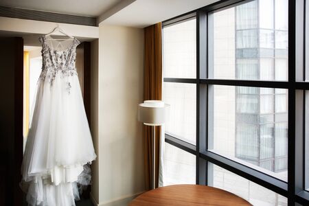 Wedding dress hanging on the wall in the room with the lamp and the window.