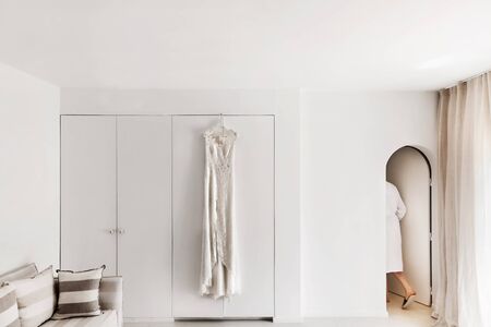 Wedding dress hanging on the wall in the white room. The bride in the dressing gown comes out and the rooms.の写真素材