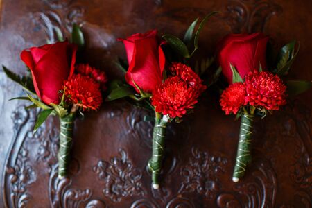 Wedding set of three boutonnieres of red roses on a leather chair.