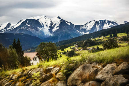 The village is in the mountains. Snow-capped mountains and forest.