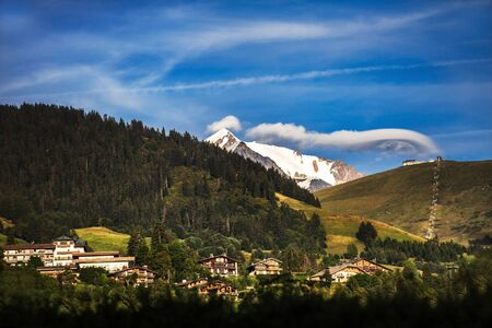 The village is in the mountains. Snow-capped mountains, clouds and forest.の写真素材