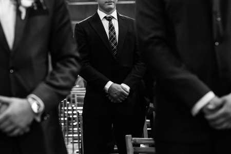 Stylish groomsmen stand during the ceremony in the church.の写真素材