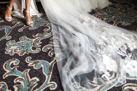 Wedding accessories. Close-up bridal shoes, legs, dress and veil, best accessories for bride for...