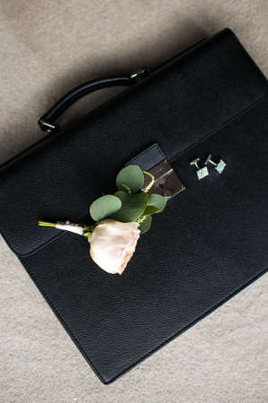 Wedding rose boutonniere and cufflinks on a leather briefcase.