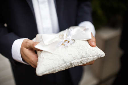 Groom holding a pillow with wedding rings.