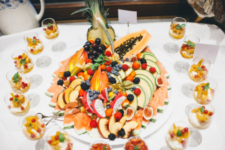 Fruits on a large round plate and glasses with desserts.の写真素材