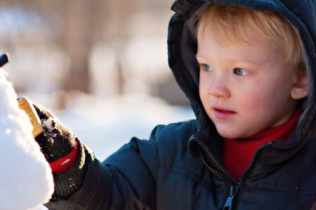 boy putting the final touches on his snowmanの写真素材