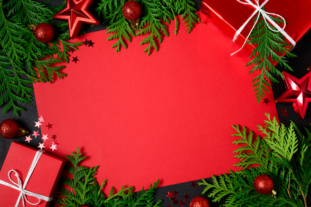 Christmas frame of red gift boxes, fir branches, confetti, paper for text and toys on black background. Flat lay. Top view. Copy spaceの写真素材