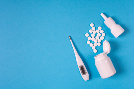 Medical electronic thermometer, medication bottle with pills and spray for nose on blue background....