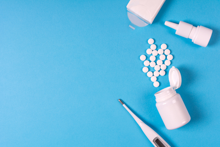 Medical electronic thermometer, medication bottle with pills and spray for nose on blue background. Health care concept. Top view. Copy space. Flat layの写真素材