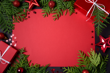 Christmas frame of red gift boxes, fir branches, confetti, paper for text and toys on black background. Flat lay. Top view. Copy spaceの写真素材
