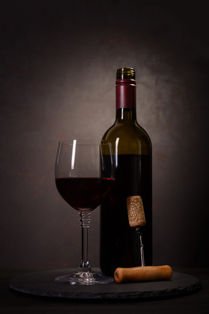 Wine bottle, glass with red wine and cork with corkscrew on dark wooden background. Celebration concept. Copy spaceの写真素材