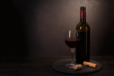 Wine bottle, glass with red wine and cork with corkscrew on dark wooden background. Celebration concept. Copy spaceの写真素材