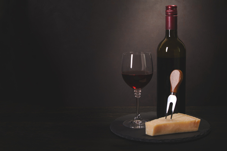 Wine bottle, glass with red wine and cheese on dark wooden background. Celebration concept. Copy space. Tonedの写真素材
