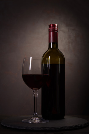 Wine bottle and glass with red wine on dark wooden background. Celebration concept. Copy spaceの写真素材