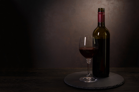 Wine bottle and glass with red wine on dark wooden background. Celebration concept. Copy spaceの写真素材