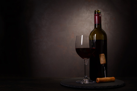 Wine bottle, glass with red wine and cork with corkscrew on dark wooden background. Celebration concept. Copy spaceの写真素材