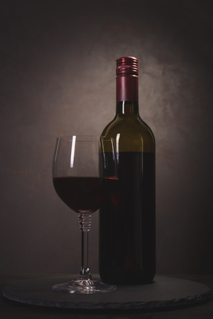 Wine bottle and glass with red wine on dark wooden background. Celebration concept. Copy space. Tonedの写真素材