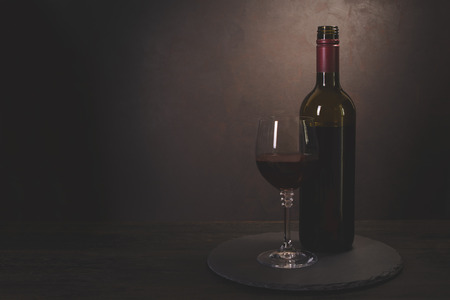 Wine bottle and glass with red wine on dark wooden background. Celebration concept. Copy space. Tonedの写真素材