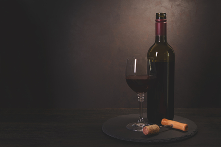 Wine bottle, glass with red wine and cork with corkscrew on dark wooden background. Celebration concept. Copy space. Tonedの写真素材