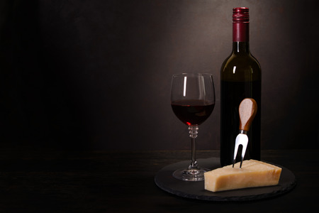 Wine bottle, glass with red wine and cheese on dark wooden background. Celebration concept. Copy spaceの写真素材