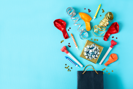 Collection of colorful birthday party objects in a gift box on blue paper background. Holiday celebration concept. Copy space. Flat layの写真素材