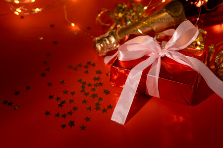 Champagne bottle with golden serpentine, garland and present box on red paper background. Valentines day, birthday, wedding celebration concept. Top view. Flat lay. Copy spaceの写真素材