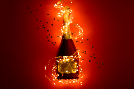 Champagne bottle wrapped in golden garland on red paper background. Valentines day, birthday, wedding celebration concept. Top view. Flat lay. Copy spaceの写真素材