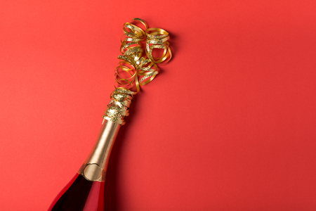 Champagne bottle with golden serpentine on red paper background. Valentines day, birthday, wedding celebration concept. Top view. Flat lay. Copy spaceの写真素材