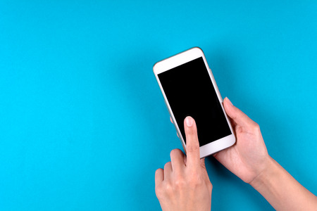 Hand touching smartphone screen on blue background. Mock-up. Top view. Copy space