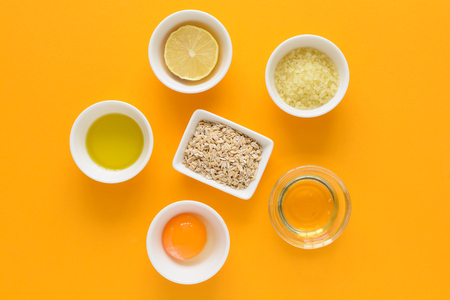 Fresh ingredients for homemade effective acne remedies on yellow background. Honey, sea salt, egg yolk, olive oil, oat, lemon and aloe. Flat lay. Copy spaceの写真素材