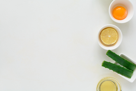 Fresh ingredients for homemade effective acne remedies on white background. Honey, sea salt, egg yolk, olive oil, oat, lemon and aloe. Flat lay. Copy spaceの写真素材