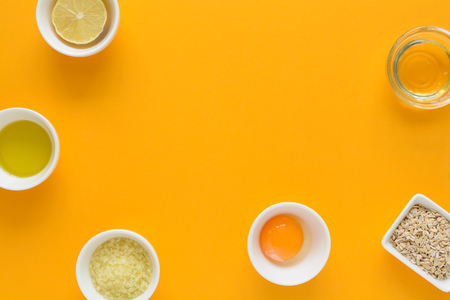 Fresh ingredients for homemade effective acne remedies on yellow background. Honey, sea salt, egg yolk, olive oil, oat, lemon and aloe. Flat lay. Copy spaceの写真素材