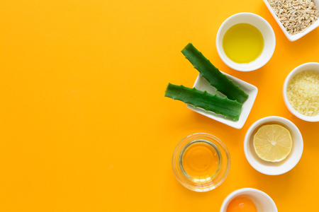 Fresh ingredients for homemade effective acne remedies on yellow background. Honey, sea salt, egg yolk, olive oil, oat, lemon and aloe. Flat lay. Copy spaceの写真素材