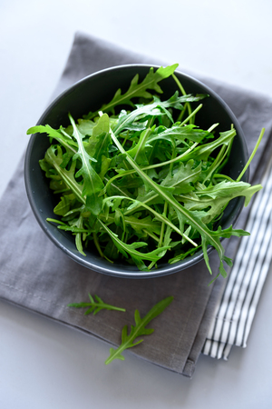 Fresh green arugula in bowl on gray wooden background. Healthy food or vegetarian concept. Top view. Copy spaceの写真素材
