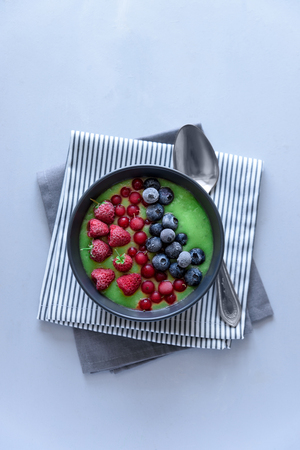 Breakfast kiwi smoothie bowl topped with frozen raspberry, blueberry and red currant on gray wooden background. Top view. Copy spaceの写真素材