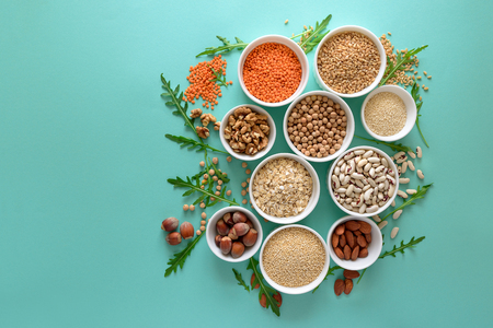 Set of bowls with organic quinoa, lentil, chickpea, wheat, walnut, almond, hazelnut and sesame. Cereals and legumes assortment on blue paper background. Top view. Copy space. Flat layの写真素材